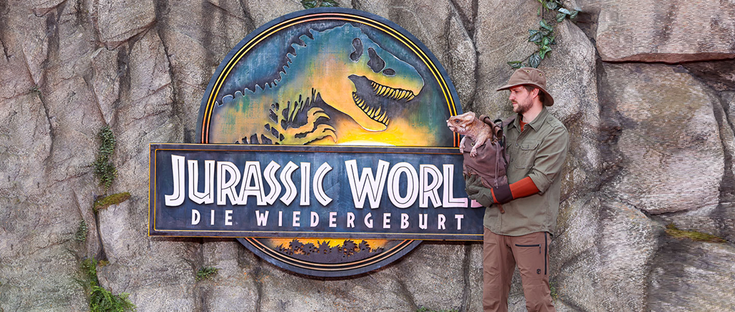 Filmlogo Jurassic World, daneben der Tierpflege mit Babydino Doloris